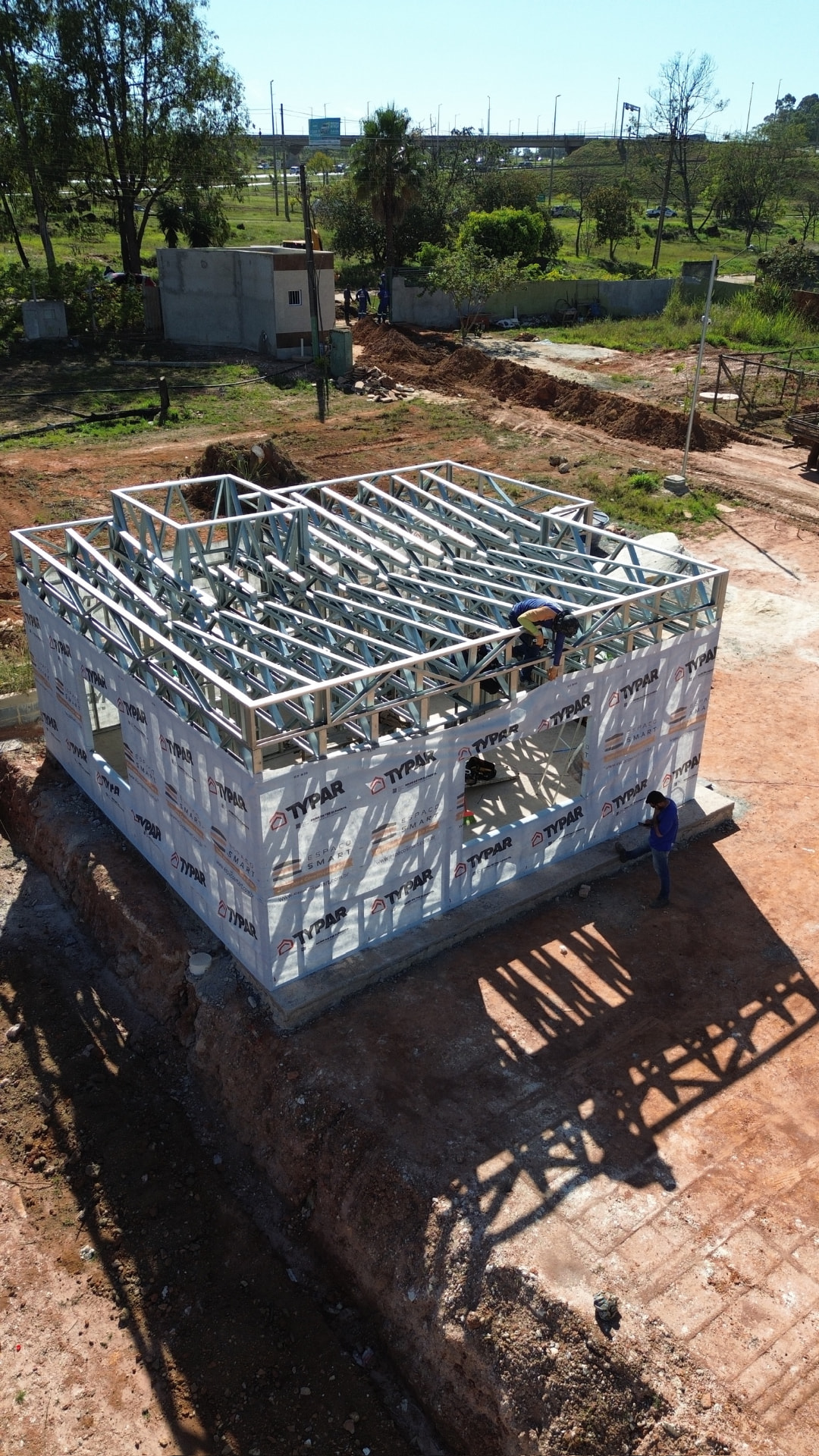 Vista aérea da estrutura em Light Steel Frame finalizada, com telhado treliçado e fechamento com manta, pronta para receber preenchimento, telhas e fechamento